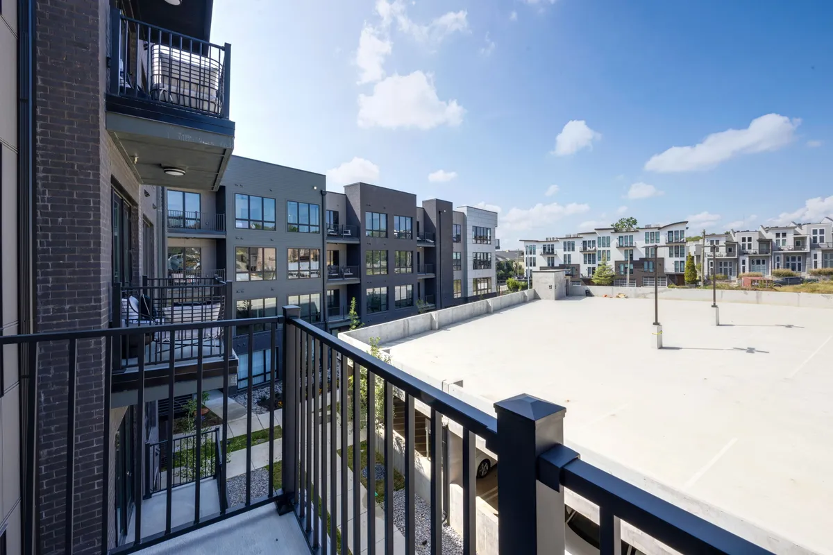 A contemporary exterior shot from a condo balcony, overlooking surrounding buildings and a dedicated open parking area. The welcoming scene suggests comfort, urban living, and ease of access, with space for socializing or unwinding outdoors after a busy day.