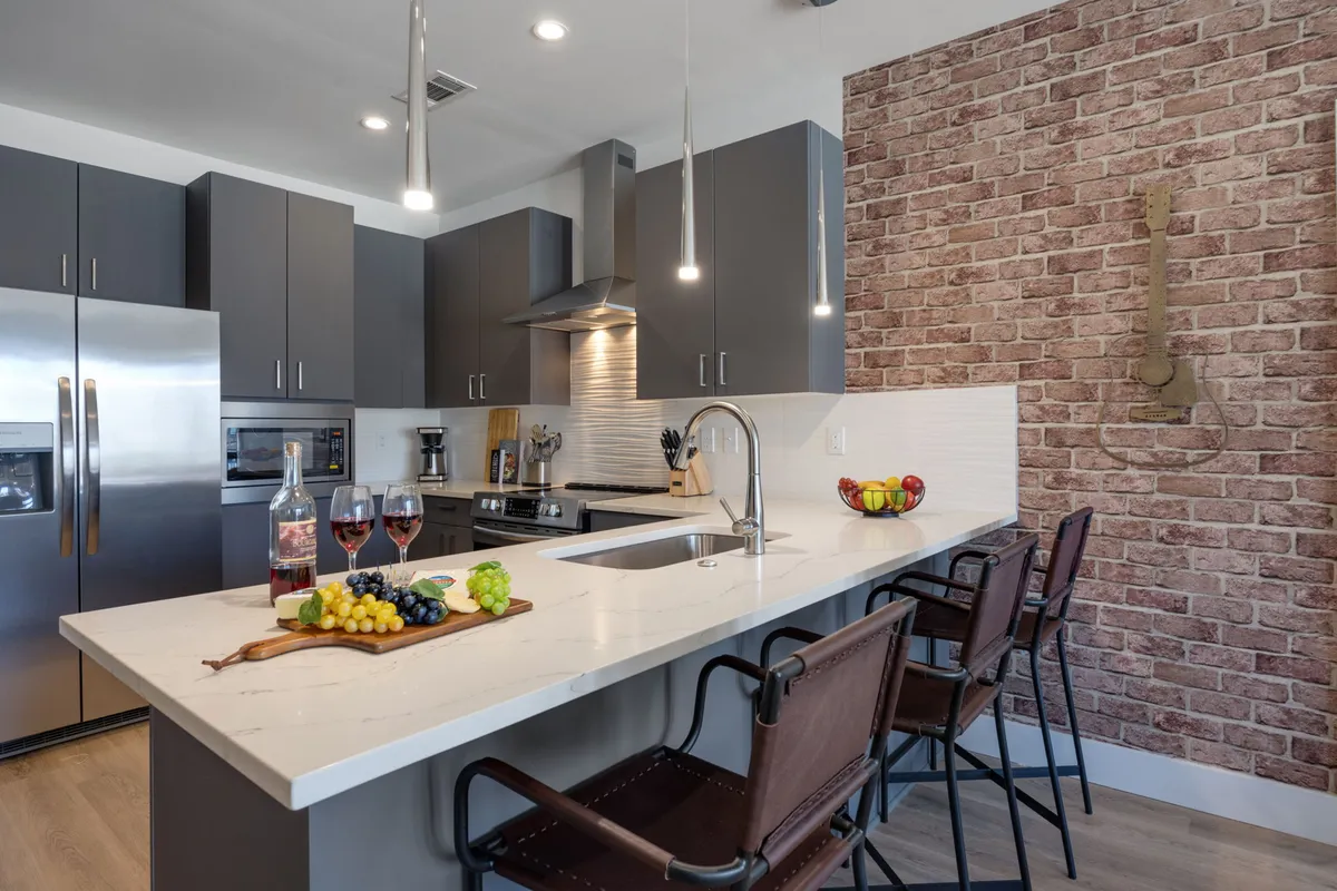 A close-up scene of the kitchen island and countertop, featuring a vibrant fruit platter, visible appliances, and a brick wall. The setup suggests a space ready for entertaining, cooking, and socializing, reinforcing a sense of warmth and hospitality.