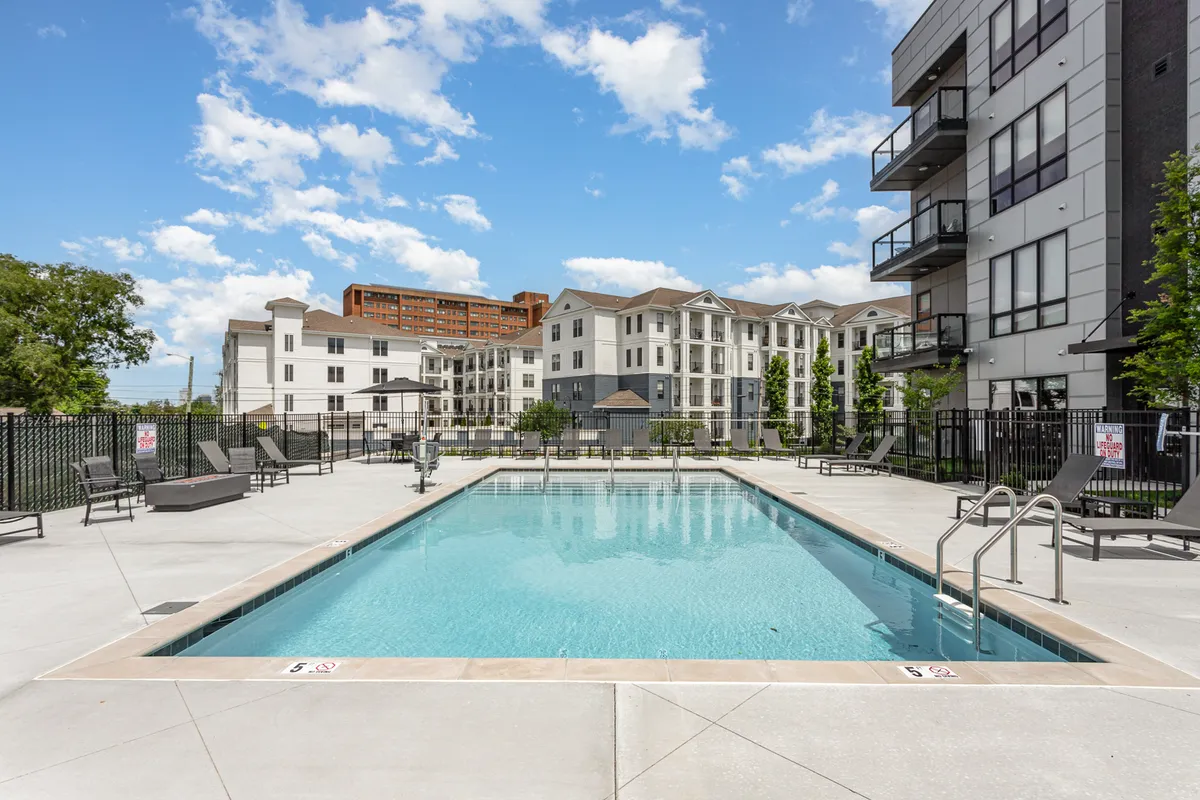 This image features a sparkling swimming pool surrounded by modern apartment buildings and lush greenery. Lounge chairs are set along the poolside, inviting residents to relax, sunbathe, or socialize in a serene outdoor setting. The ambiance is enhanced by a sense of community and leisure, with ample space for gatherings and recreation.